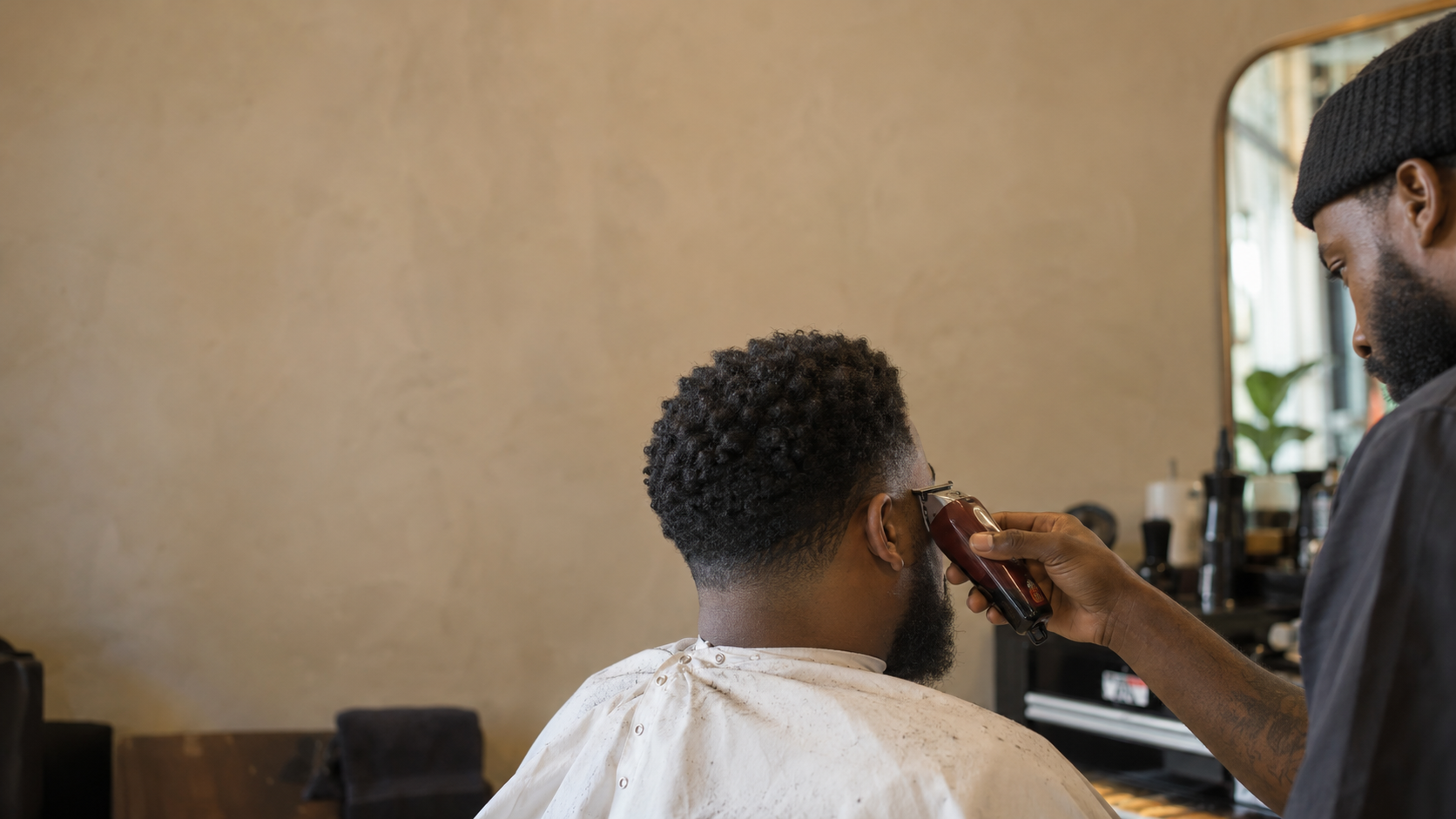 A barber carefully tapering a client's natural textured hair in a sunlit salon